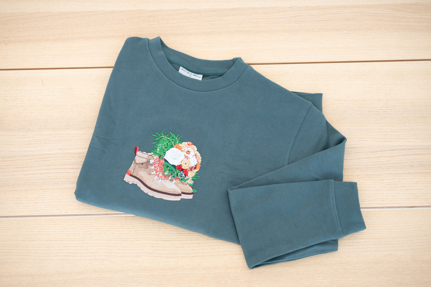 Custom embroidered crewneck in forest green laid flat showing floral boot design