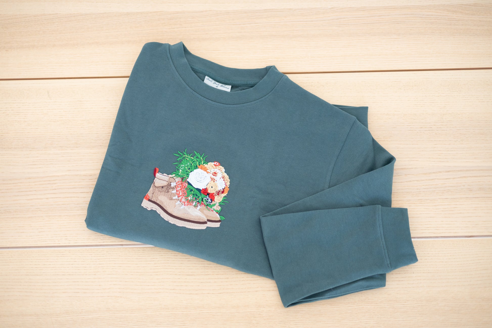 Custom embroidered crewneck in forest green laid flat showing floral boot design
