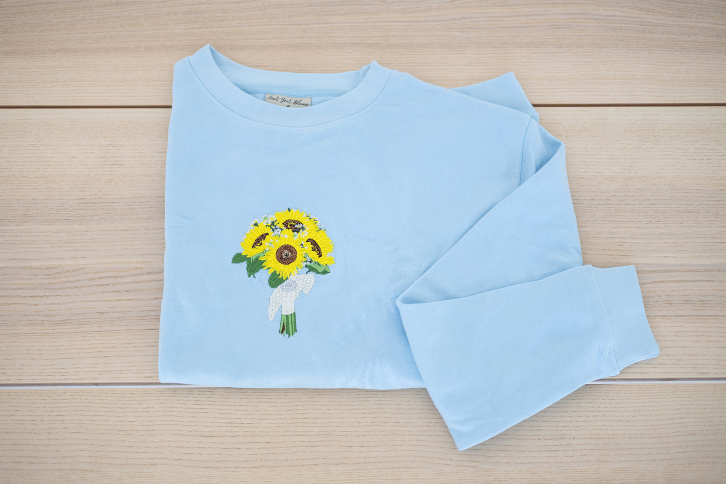 Embroidered wedding bouquet crewneck in light blue laid flat showing sunflower design