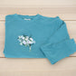 Custom floral embroidery with white roses and greenery on mint crewneck laid flat