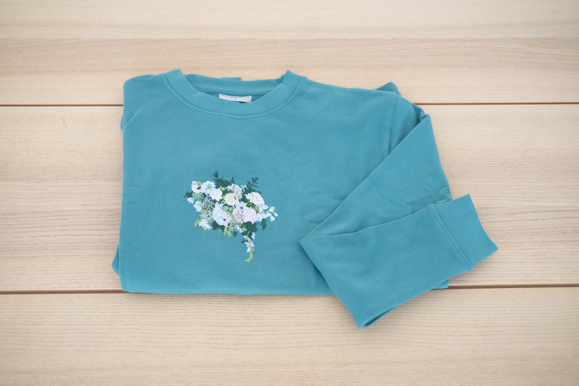 Custom floral embroidery with white roses and greenery on mint crewneck laid flat